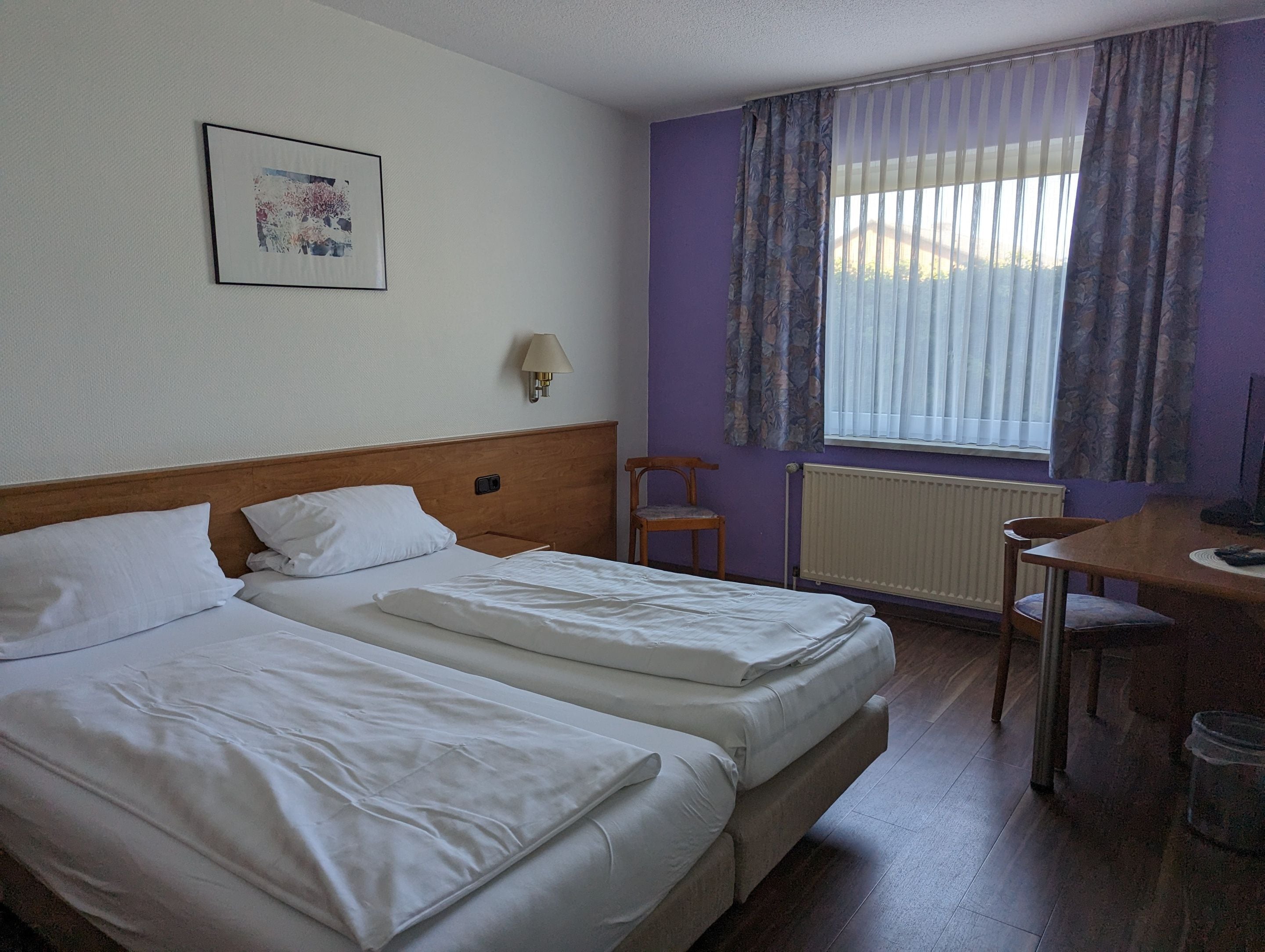 A hotel room with two beds, a desk, a chair, a lamp, and a window with curtains.