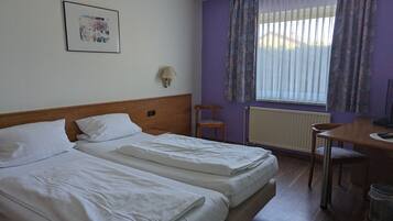 A hotel room with two beds, a desk, a chair, a lamp, and a window with curtains.