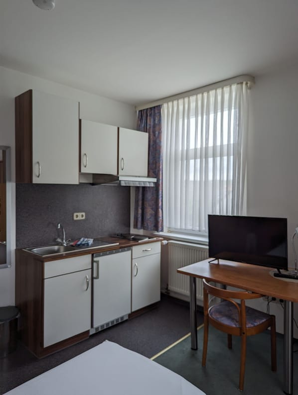 A compact kitchen with white cabinets, a built-in stove, and a window with sheer curtains.