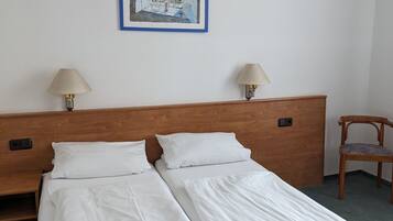 Una habitación de hotel con una cama doble, dos lámparas de noche, un cabecero de madera, un cuadro enmarcado en la pared y una silla de madera.