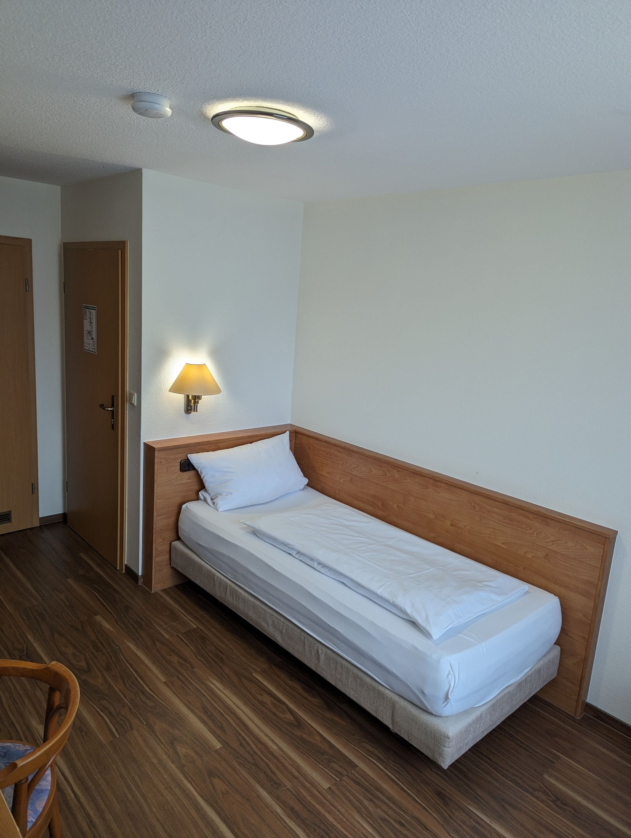 Ein Einzelbett mit Holzkopfstück, eine Wandlampe und eine Tür mit einem Schild.