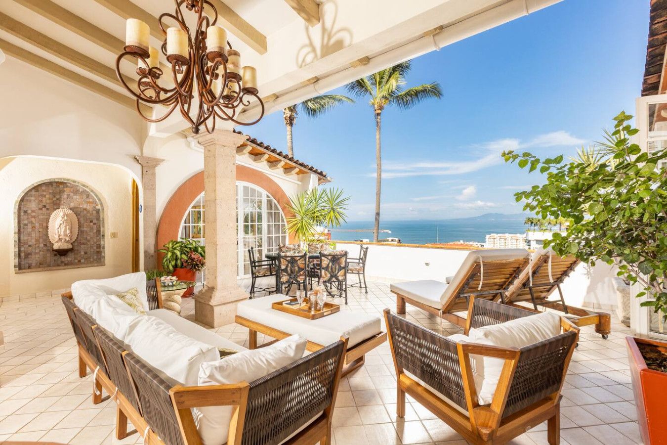 A sunlit patio with wicker furniture, a stone fireplace, and a view of the sea.
