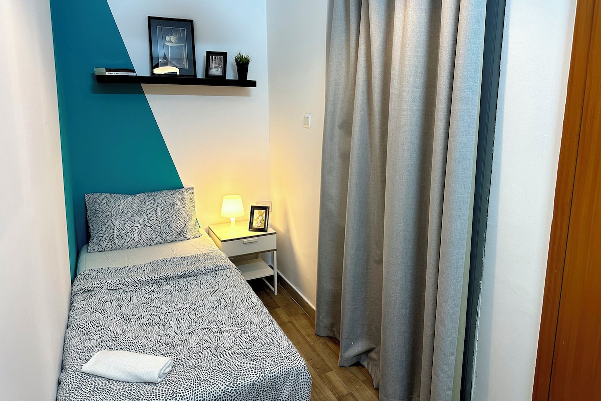Een slaapkamer met een bed, nachtkastje, lamp en een plank met ingelijste foto’s.