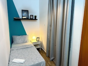 Een slaapkamer met een bed, nachtkastje, lamp en een plank met ingelijste foto’s.