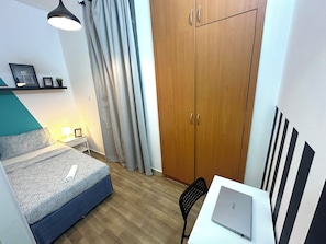 Een slaapkamer met een bed, een bureau met een laptop, een kledingkast en een hanglamp.