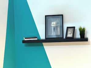 A shelf with a framed picture, a small potted plant, and a book. - Cityscape Partition Room in Tecom (Dubai)