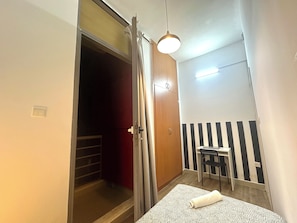 A bedroom with a bed, a desk, a chair, a wardrobe, and a hanging light fixture. - Cityscape Partition Room in Tecom (Dubai)