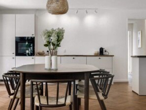 A modern kitchen with white cabinetry, a round dining table with chairs, and a hanging light fixture. - 12 Person Holiday Home in Vejby (Vejby)