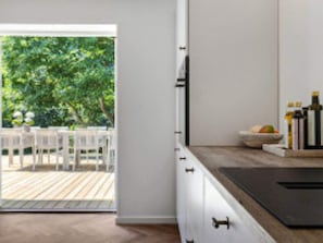 A modern kitchen with a wooden countertop, white cabinets, and a view of an outdoor deck. - 12 Person Holiday Home in Vejby (Vejby)