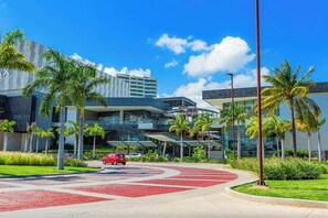 A modern hotel with a curved driveway, palm trees, and a clear blue sky. - 2BR Puerto Cancun With Rooftop Pool, Gym & Marina (Cancun)