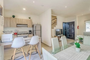 A modern kitchen with a gas stove, refrigerator, and microwave. There is a dining area with a glass table and white chairs. - 3BR Villa - Playa del Carmen - Pool - Sleeps 7 (Playa del Carmen)