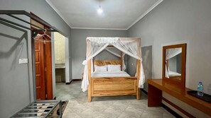 Ein Zimmer mit einem hölzernen Bett, einem Nachttisch, einem Spiegel und einer Tür zu einem anderen Raum.