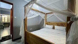 Ein Einzelbett mit Holzbettgestell und weißer Bettwäsche, einem Holz-Kopfstück und einem Moskitonetz.