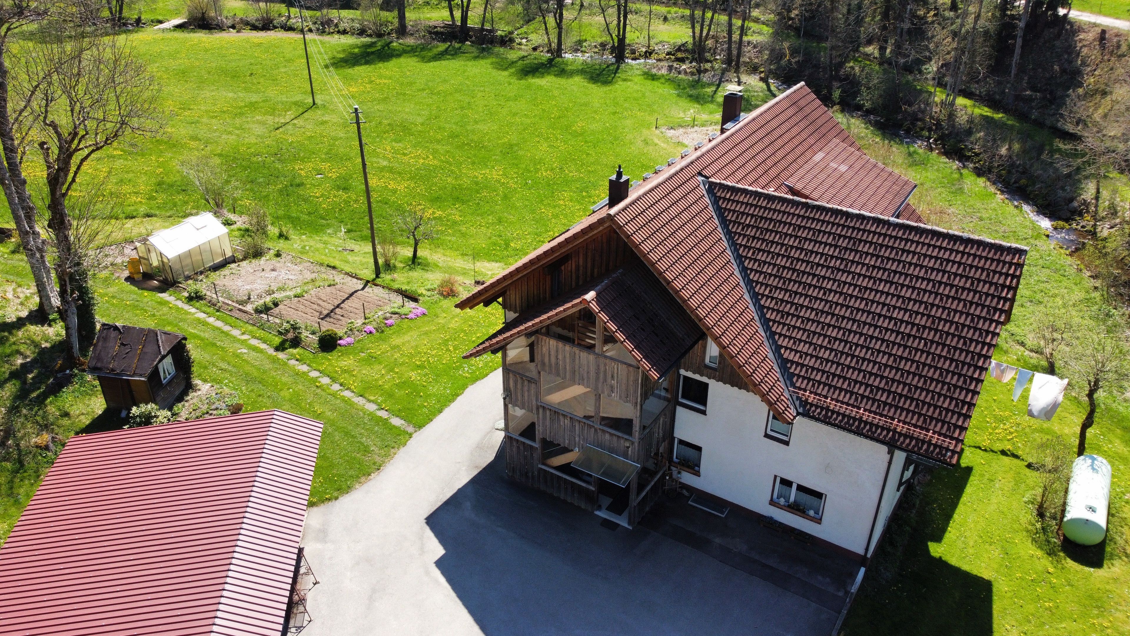 Ein zweigeschossiges Haus mit einem geneigten Dach, einer Veranda und einem Garten mit einem Gewächshaus.