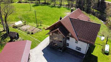 Ein zweigeschossiges Haus mit einem geneigten Dach, einer Veranda und einem Garten mit einem Gewächshaus.