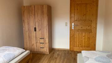 A room with a wooden wardrobe, two beds with patterned bedding, and a wooden door.