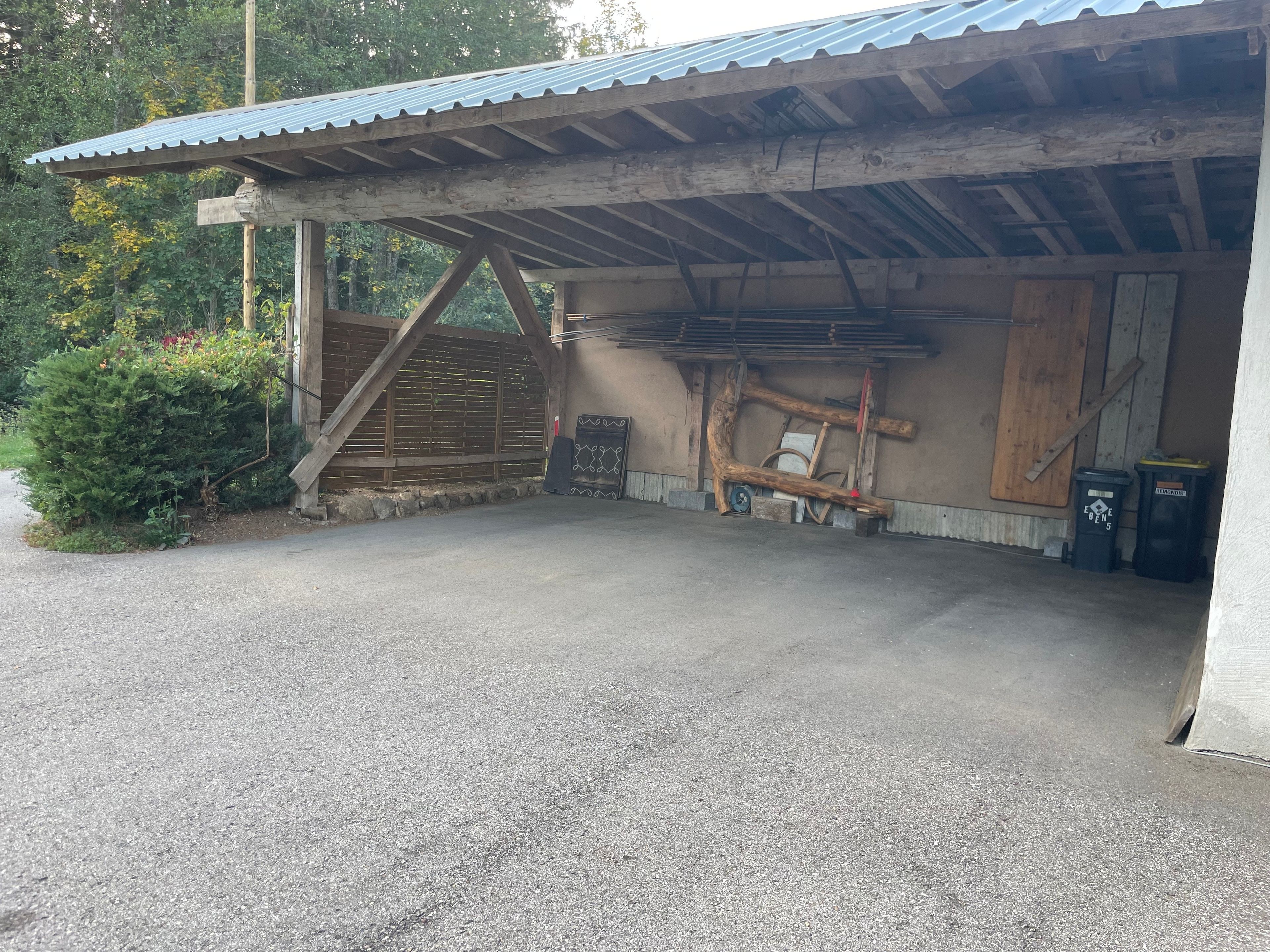 Eine Garage mit Überdachung, Metalldeckung, Holzbalken und Betonboden.