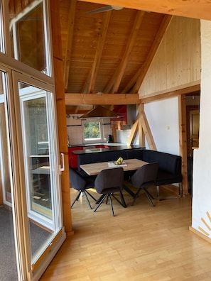 Et moderne køkken med en central ø, træbjælker og et spiseområde med bord og stole.