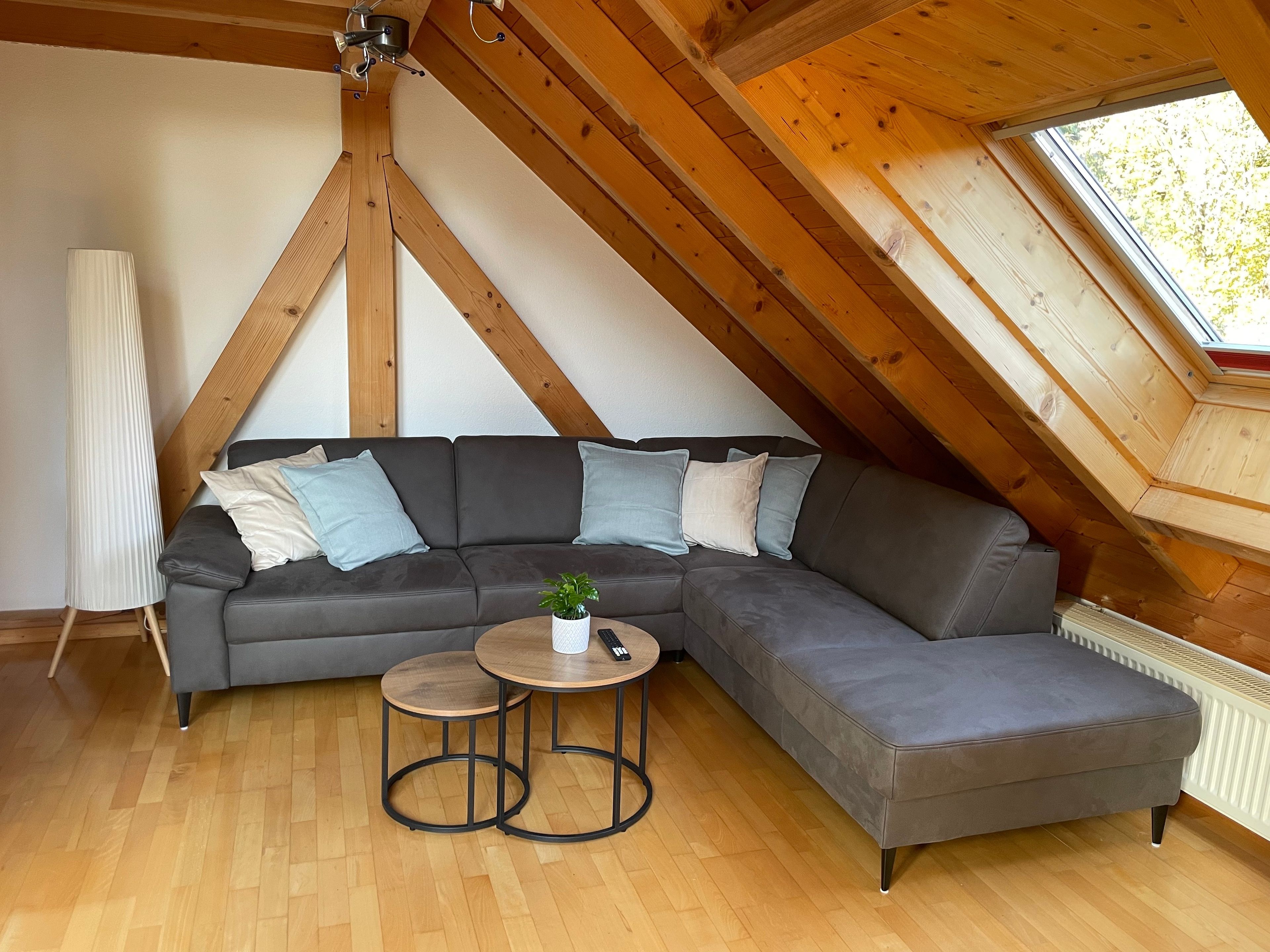 Une chambre de style loft moderne, dotée d’un grand canapé d’angle, d’une petite table ronde et d’une lucarne.