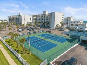 A multi-story hotel with a tennis court and parking area. - Smyrna Beach Club 218B 🌊 Oceanfront Condo with Private Balcony (New Smyrna Beach)