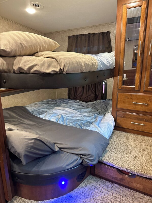 Un lit superposé avec un lit inférieur, une armoire en bois avec des tiroirs et une bouche d’aération au plafond.