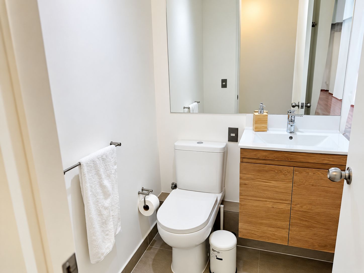 A modern bathroom with a toilet, sink, mirror, and a white towel on a rack.