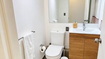 A modern bathroom with a toilet, sink, mirror, and a white towel on a rack.