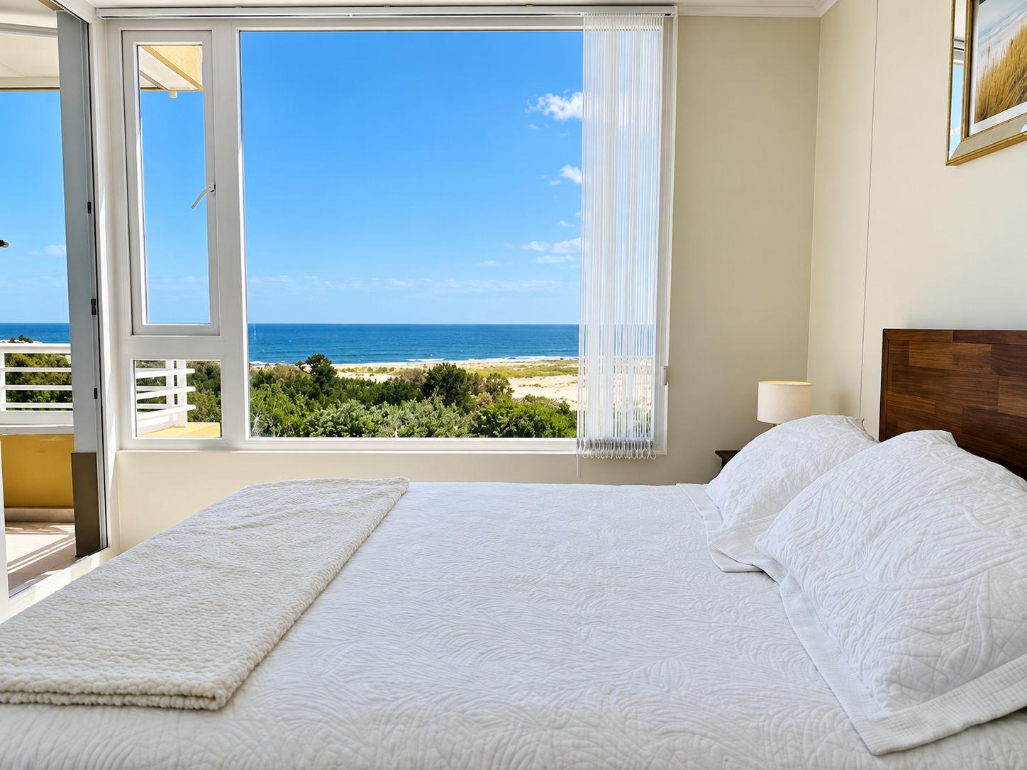 A bedroom with a bed, a view of the beach, and a balcony.