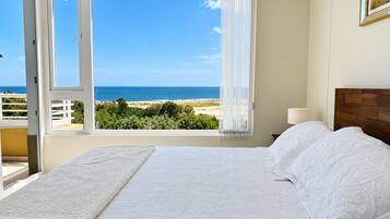 A bedroom with a bed, a view of the beach, and a balcony.