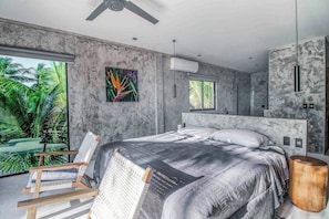 A modern bedroom with a large bed, a ceiling fan, and a view of palm trees. - Beachfront Home Private Pool, Jacuzzi, Sauna (Tulum)