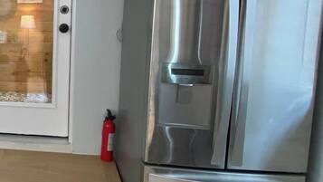 Un refrigerador de acero inoxidable con dispensador de agua, un extintor y una puerta con panel de vidrio.