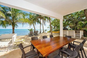 Ein Holztisch mit Stühlen im Freien, mit Blick auf das Meer und Palmen.