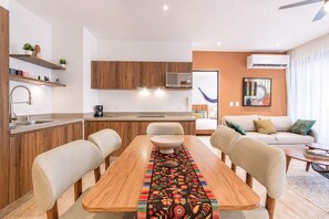 A modern kitchen with wooden cabinets, a dining area with a wooden table and chairs, a sofa, and a small coffee table. - Ceiba 25 Rooftop Pool, Gym & 5th Ave Condo (Playa del Carmen)