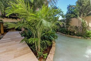 A pool area with a wooden deck, surrounded by lush greenery and a clear water feature. - Centro Playa Studio - Rooftop Pool & Gym (Playa del Carmen)