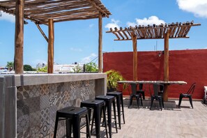 Eine Terrassengaststätte mit Holz-Pergola, einer Bar mit Hockern und einer roten Wand im Hintergrund.