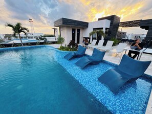 A modern outdoor pool area with lounge chairs and a building with a flat roof. - Ground-floor Studio · Terrace · Near 5th Ave (Playa del Carmen)