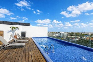A rooftop pool with lounge chairs, a palm tree, and a city view. - Icono Ocean-view Condo Rooftop Pool, Playa (Playa del Carmen)