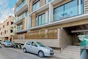 A modern multi-story building with a car parked in front. - Icono Ocean-view Condo Rooftop Pool, Playa (Playa del Carmen)