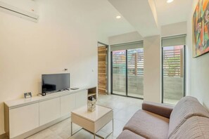 A modern living room with a flat-screen TV, a sofa, a coffee table, and a sliding glass door leading to a balcony. - Icono Ocean-view Condo Rooftop Pool, Playa (Playa del Carmen)