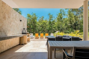 An outdoor patio with a stone wall, seating area, and a view of the surrounding greenery. - Luxury Xpu-ha Villa: Private Pool, 5 Bedrooms (Xpu-Ha)