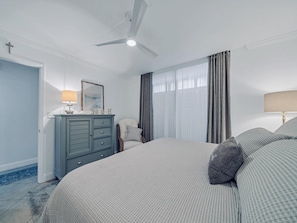 A bedroom with a bed, a dresser, a chair, a ceiling fan, and a window with curtains. - Destin Pointe Magnolia House #306 (Destin)