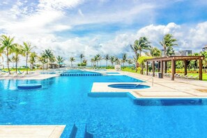 A swimming pool with multiple lanes, surrounded by palm trees and a covered seating area. - Mareazul Beachfront 2BR Pool & Sea Views (Playa del Carmen)
