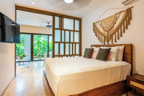 A bedroom with a large bed, a TV mounted on the wall, and a view of the outdoors. - Modern 1BR Condo - Rooftop Pool & Gym (Playa del Carmen)