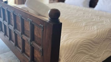 Una cama de madera con cabecera, una colcha estampada y una mesita de noche con lámpara.