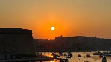 Un puerto al atardecer con barcos amarrados y un paisaje urbano al fondo.