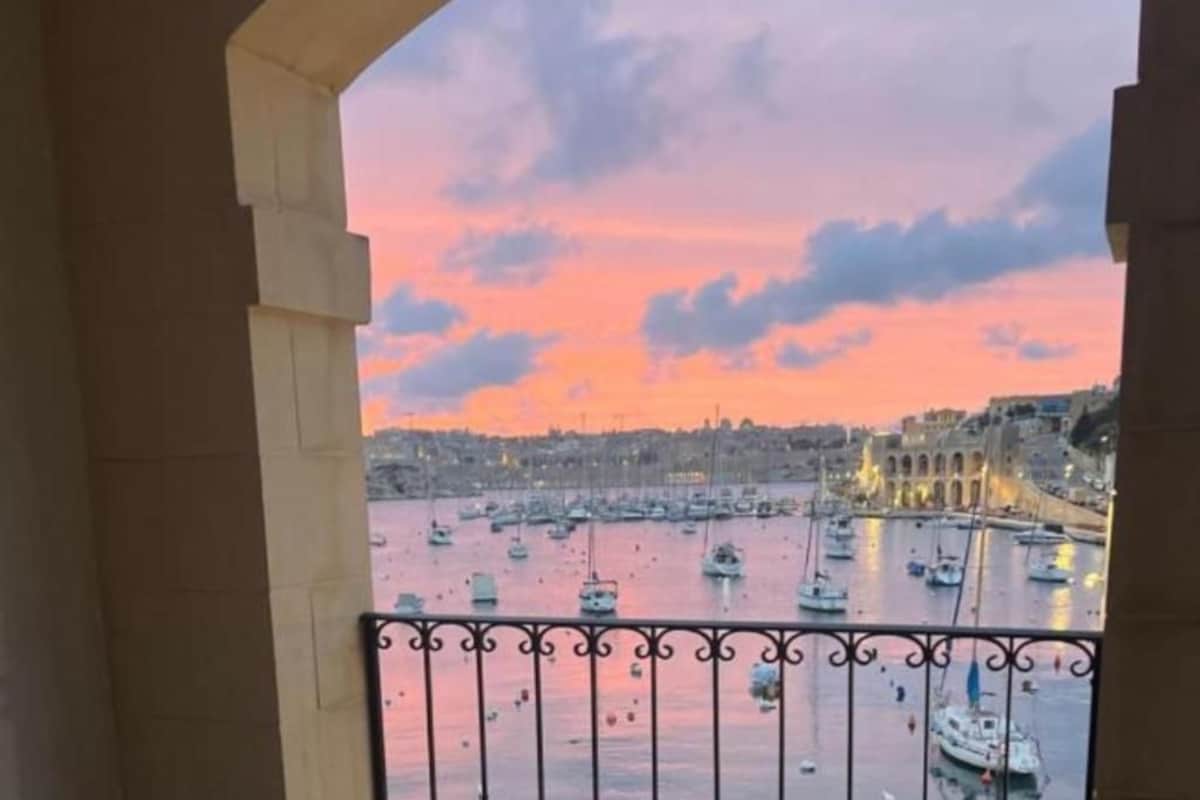 Ein Balkon mit Blick auf einen Hafen bei Sonnenuntergang, mit Booten und Gebäuden.
