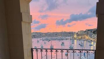 Un balcón con vistas a un puerto al atardecer, con barcos y edificios.