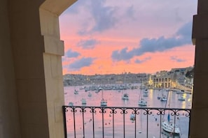 Ein Balkon mit Blick auf einen Hafen bei Sonnenuntergang, mit Booten und Gebäuden.