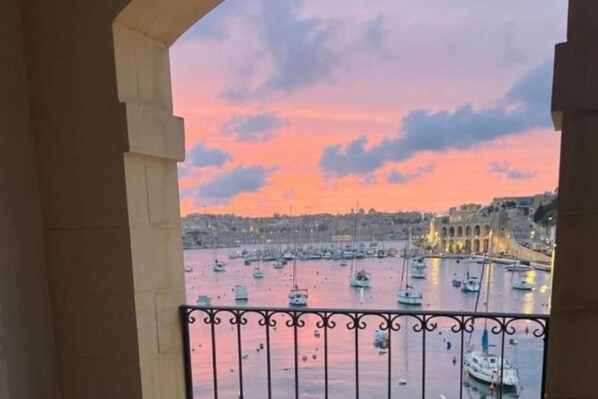 Un balcón con vistas a un puerto al atardecer, con barcos y edificios.