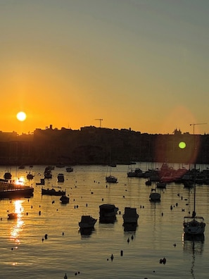 A harbor at sunset with boats and a distant cityscape. - Front Row Malta - Waterfront Home    (Kalkara)